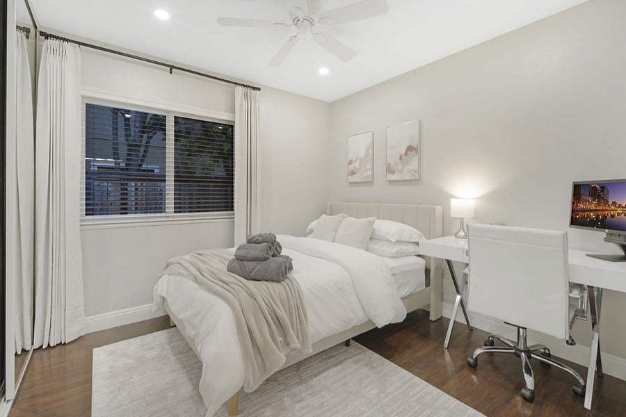 The bedroom features a cozy full-size bed with blackout curtains for restful sleep. A desk with a laptop monitor and an ergonomic office chair provides a perfect workspace. The spacious closet comes with hangers, offering ample storage.
