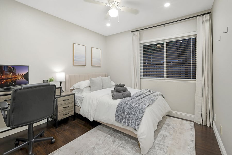 This bedroom includes a comfortable full-size bed with blackout curtains for complete darkness. It has a desk with a laptop monitor and an office chair for a productive workspace. A spacious closet with hangers provides ample storage for clothes.