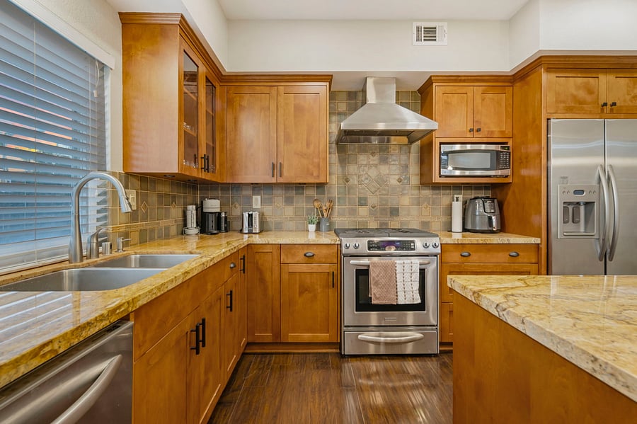 A sleek kitchen gleams with stainless steel appliances, including a side-by-side fridge and a 30 gas range with oven. Granite countertops and a large island offer ample prep space. Cabinets are filled with elegant dishware, cookware, and utensils.