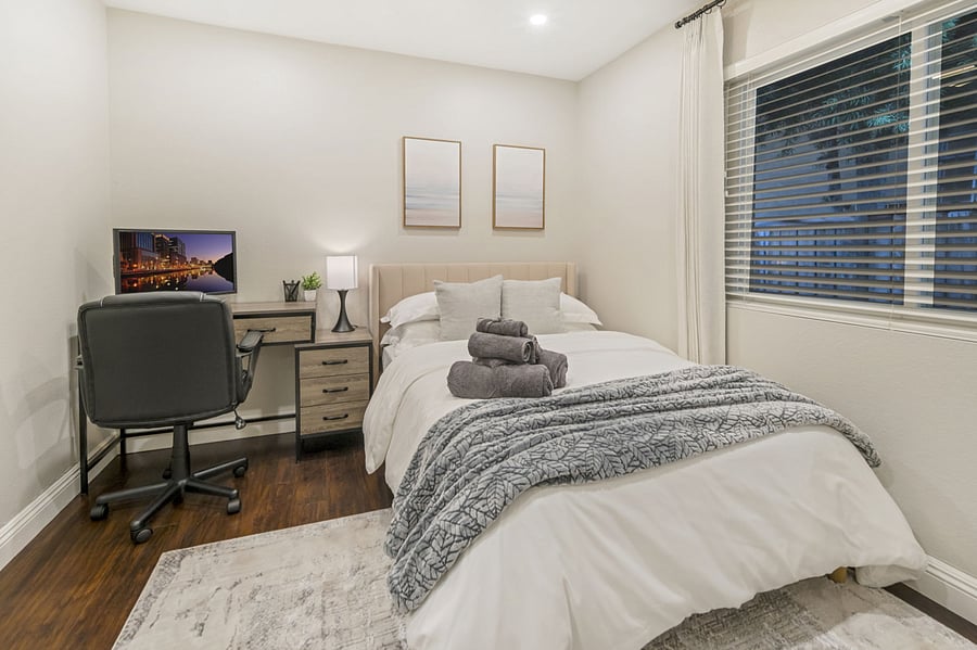 This bedroom features a desk perfect for productivity, paired with a laptop and monitor for dual-screen convenience. An ergonomic office chair ensures comfort during long work sessions, creating an ideal workspace within the cozy bedroom setting.