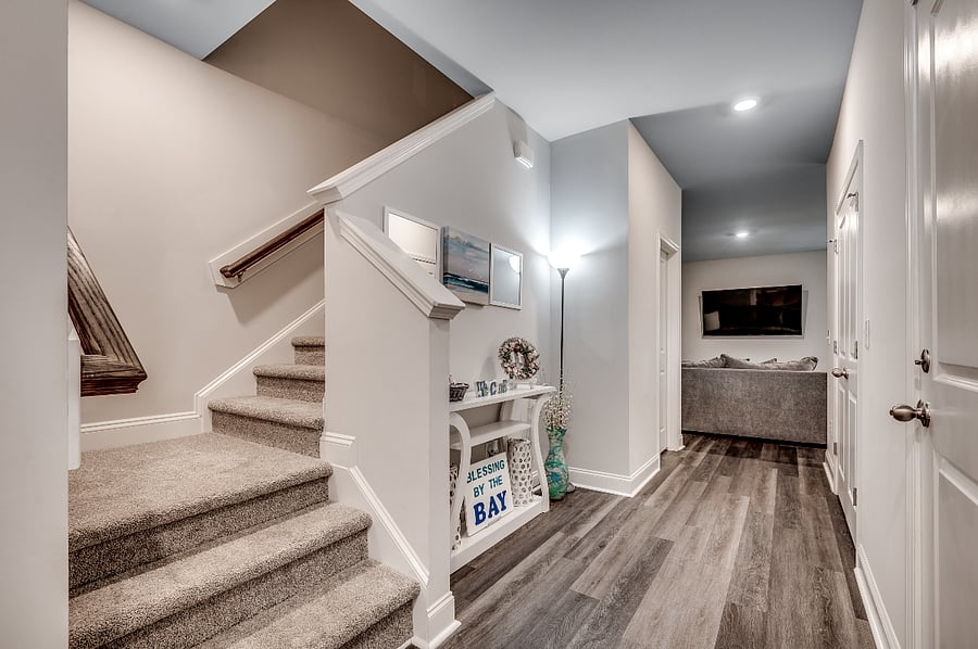 Welcoming entrance hallway with sleek vinyl plank flooring, stairs leading to the second floor on the left, and a glimpse of the inviting main floor living area ahead.