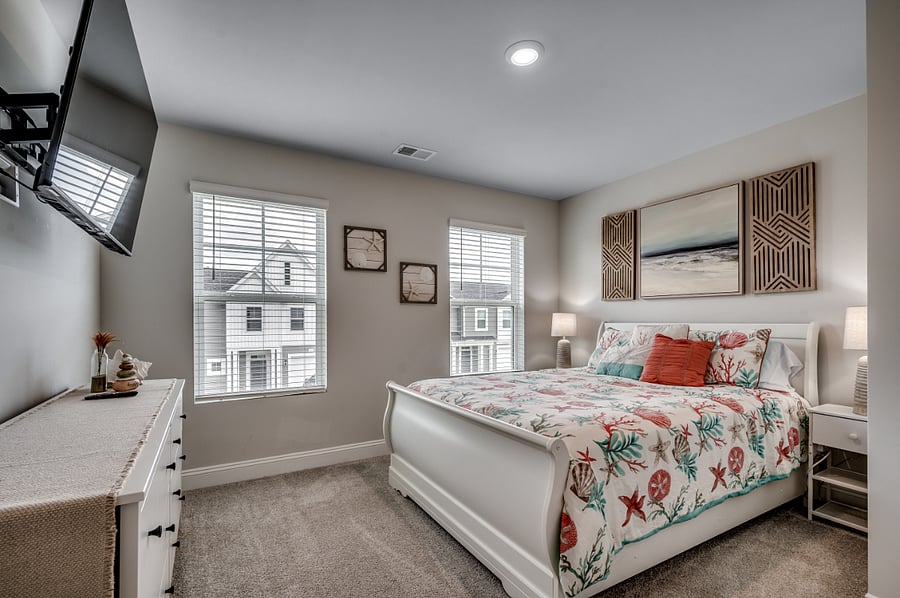 Charming second bedroom with a beach theme, featuring a queen bed, smart TV, large dresser, dual side tables, and plenty of natural light.