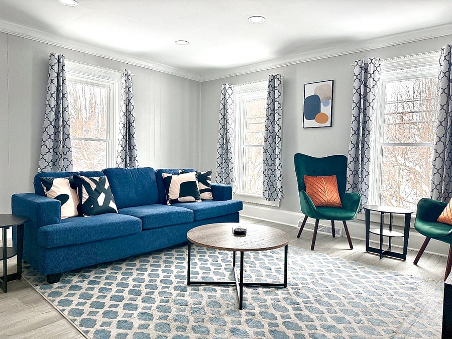 This bright and airy living room features a deep, large comfortable sofa paired with two stylish accent chairs, creating a perfect spot to relax and unwind in a welcoming atmosphere. All windows are equipped with blackout shades, giving you the flexibility to control the lighting and maintain privacy whenever you wish.