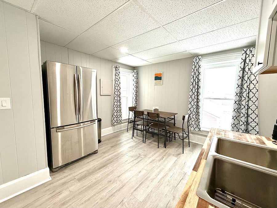 This fully equipped kitchen features a sleek full-size French door stainless steel fridge, perfect for storing all your essentials. The dining area includes a table with chairs and a cozy bench in the corner, creating a welcoming space for meals and gatherings.