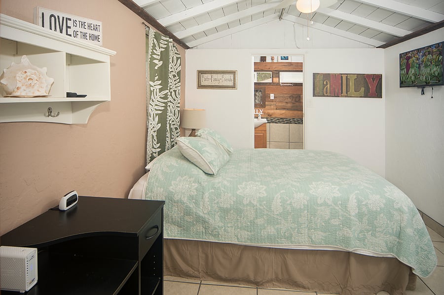 Queen bed with flat screen on the right wall and A/C and desk to the left