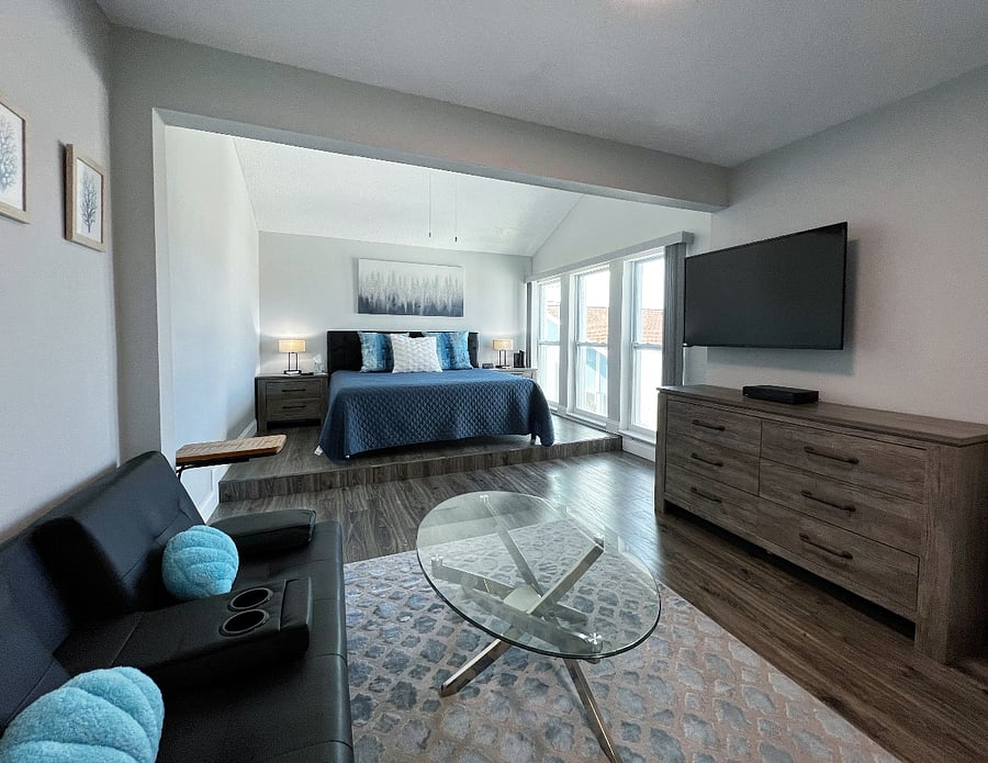 Master suite with a king sized bed, room darkening shades, a smart TV that swivels to face the bed, walk in closet, and a sitting area.