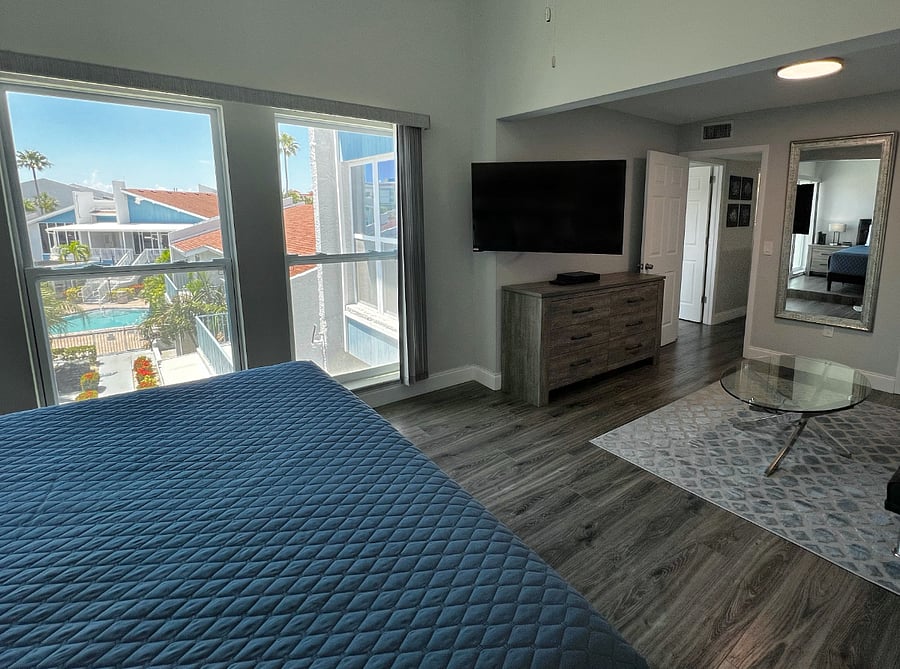 Master suite with a king sized bed, room darkening shades, a smart TV that swivels to face the bed, walk in closet, and a sitting area.