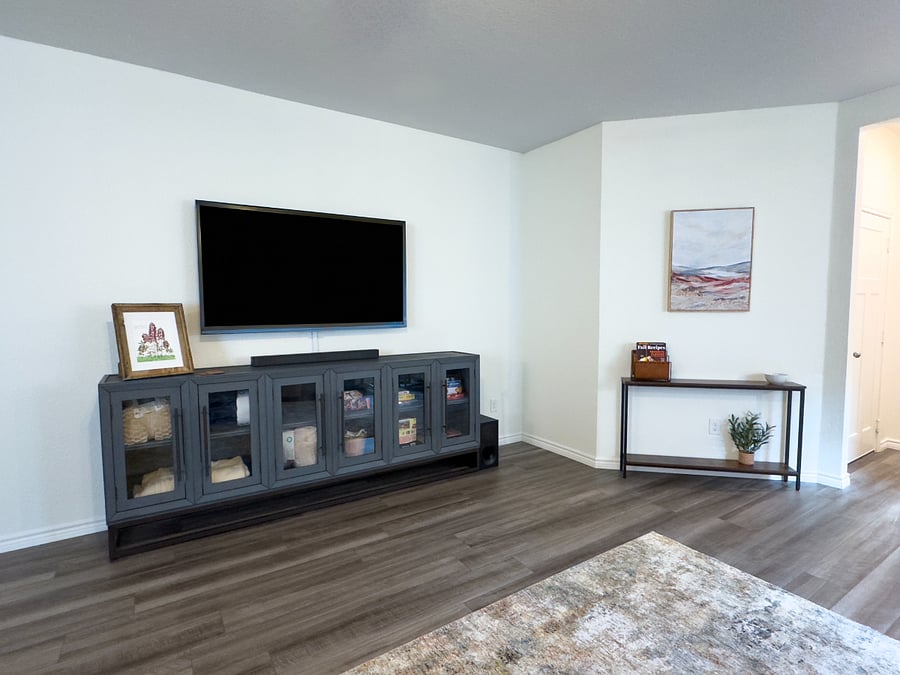 Huge TV over console filled with throw blankets, a deck of cards, and other games.