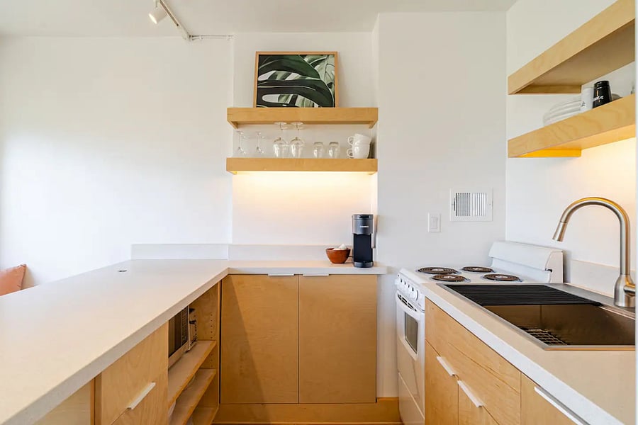 Full kitchen with custom birch cabinetry, quartz counters, open shelving, and under-cabinet lighting.