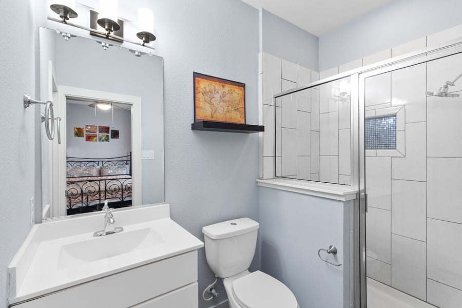 A fully equipped, clean ensuite bathroom featuring a large glass walk-in shower, ample vanity space, and modern lighting just steps from your queen bed.