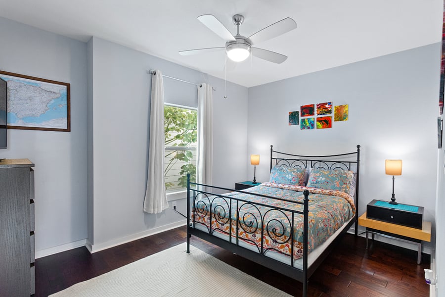 Relax in a bright, beautifully styled bedroom featuring a comfortable queen bed, warm bedside lighting, and a refreshing ceiling fan. A large window brings in lovely natural light.