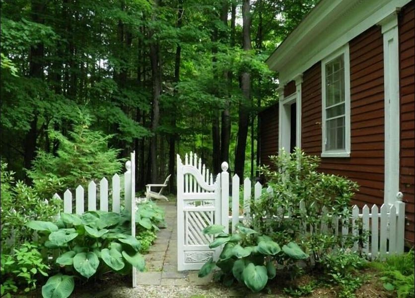 Picturesque antique garden gate leading to fire pit and easy chairs, BBQ and metal table for four.