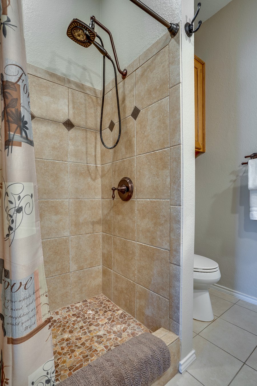 The master bathroom has a large custom-tiled step-in shower with a hand-held shower head and a large stationary shower head.