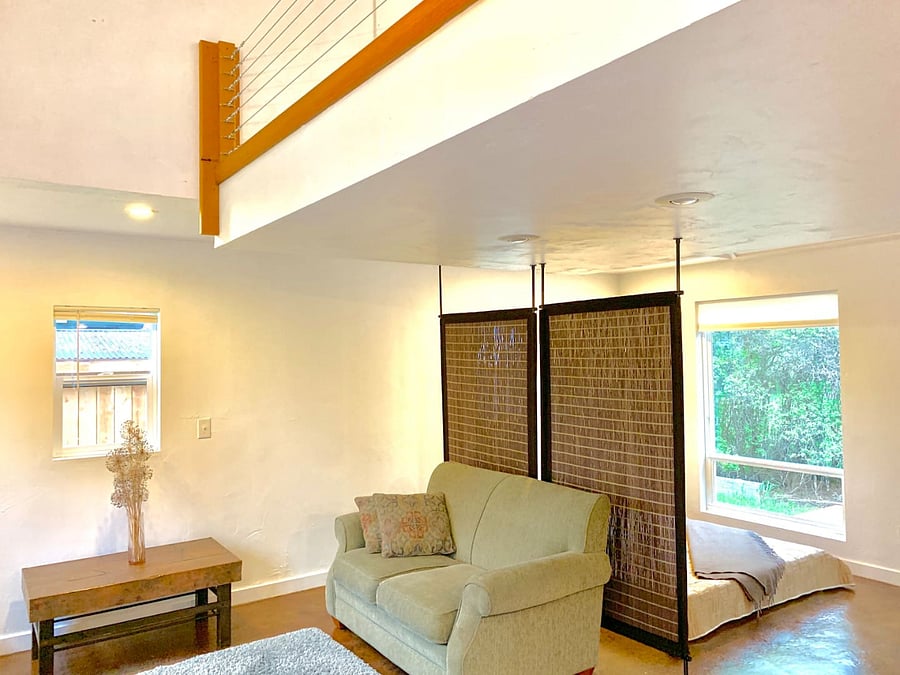 Living space and south-facing windows. Sleeping area and queen bed to the right of the privacy screen.