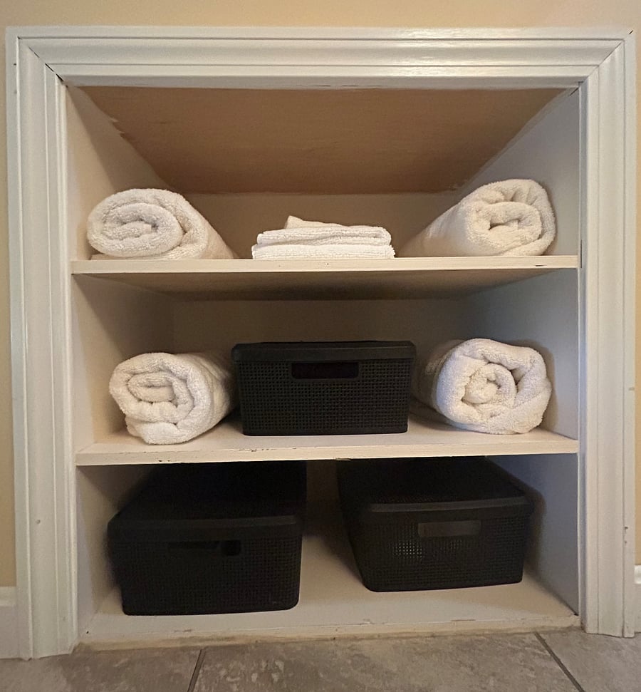 Shelves for storage, including plush towels, hand towels and washcloths, and floor mats available for use.