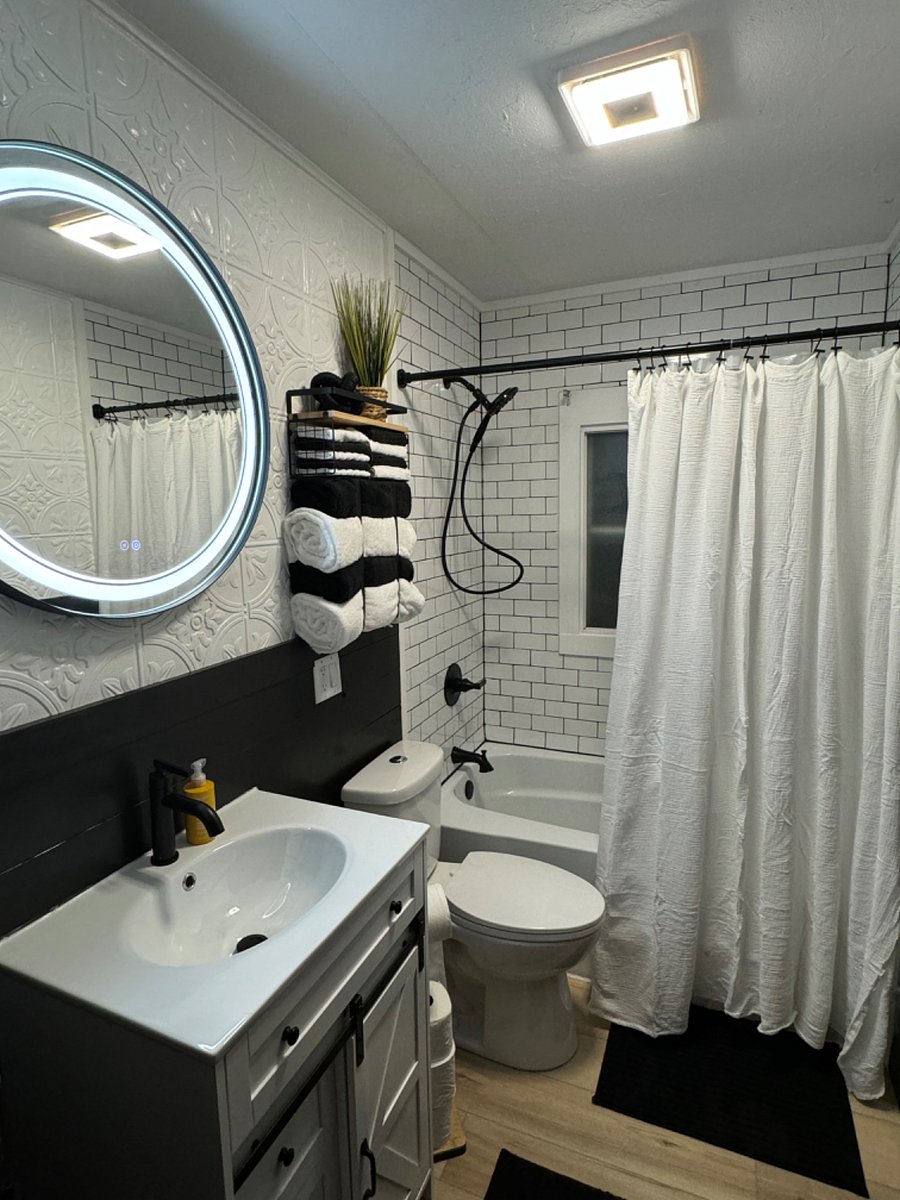 Bathroom with lighted mirror, deep tub, subway tile and shower head with handle.