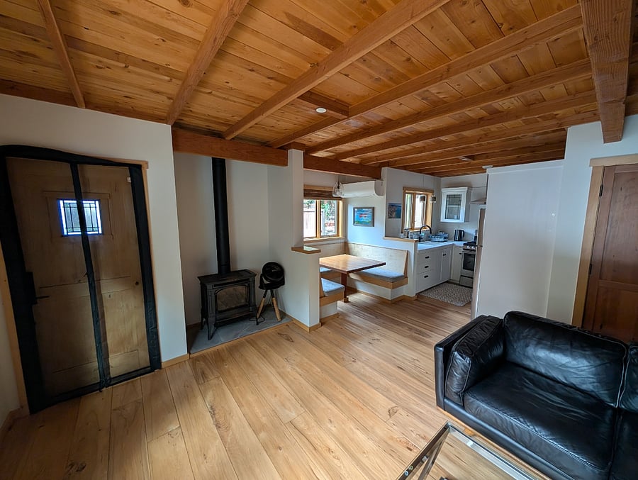 View looking towards the front door from the living room.  The front door has a screen on it.  You can also see the gas potbelly heater with the black pipe above it 