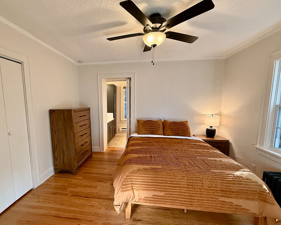 Second Bedroom with Queen Bed, En-Suite Full Bathroom, Walk-In Closet, Black Out Curtains, Dresser, Nightstand, and Bedside Lamp.