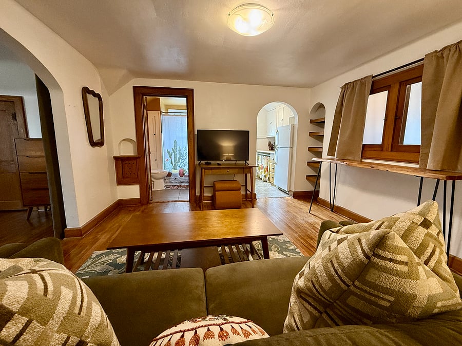 Living Room looking towards the Kitchen (right archway), Full bathroom (left of TV), and Bedroom (left archway).
