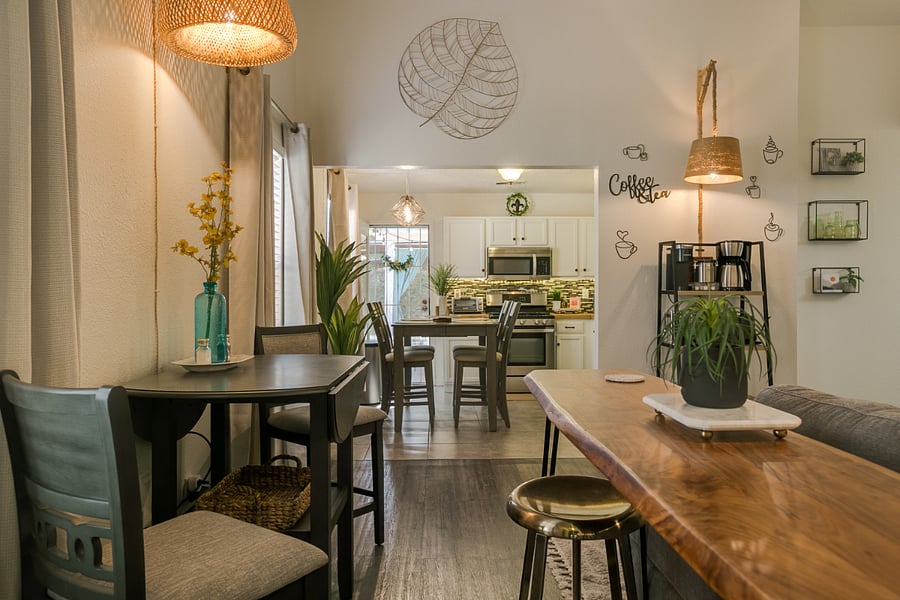 This space presents a warm and inviting open-concept dining and kitchen area, ideal for comfortable and stylish living. Key features include:
1. Dining Area: A cozy table with seating for four, perfect for meals or working from home. Decor elements like a tall vase with yellow floral accents add a touch of color.
2. Kitchen: Visible in the background, the kitchen is equipped with stainless steel appliances, ample counter space, and a modern backsplash. The area is well-lit, enhancing its functionality and aesthetic.
3. Natural Elements: The room includes several potted plants, adding vibrancy and a refreshing atmosphere. The wooden accents, such as the live-edge wood countertop, bring warmth and a rustic feel to the space.
4. Coffee Bar: A dedicated coffee nook features a rack with a coffee maker and mugs, offering a welcoming touch for caffeine lovers.
5. Lighting: A mix of overhead and wall lighting enhances the ambiance, with pendant lights that lend a modern touch.
This space is well-suited for individuals or small groups seeking a comfortable, functional, and aesthetically pleasing environment. Ideal for midterm rentals, it combines style and practicality.