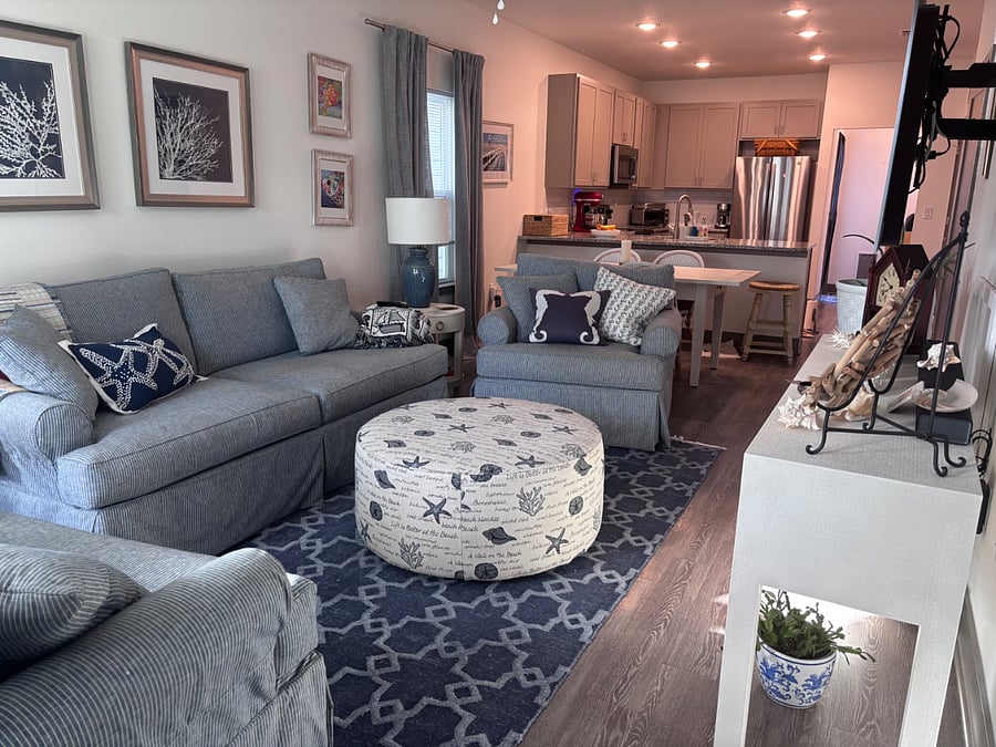 Charming coastal-themed interior, including smart TV, comfortable couch, two love seats, full dining table, bar, kitchen, and access to back yard.