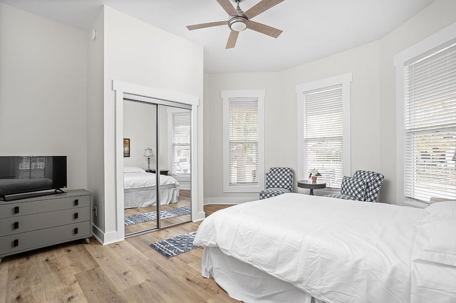 Bright and airy bedroom with a cozy bed, mirrored closet, and a charming seating area by the windows.