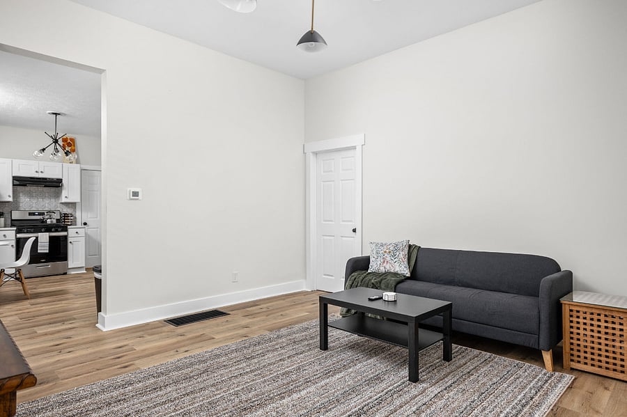 Bright and modern living room with a black sofa, sleek coffee table, and open layout leading to the kitchen.