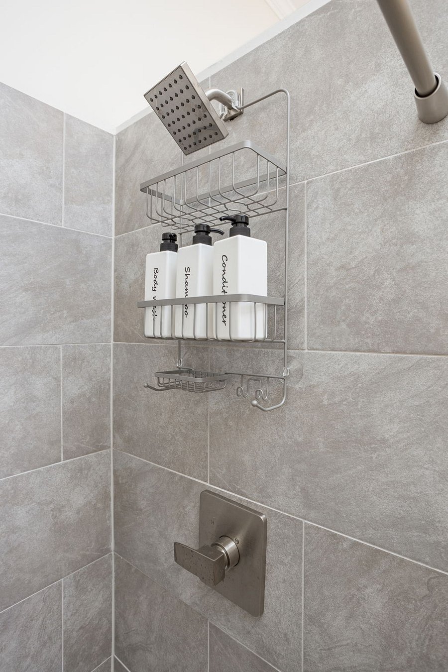 Modern shower space with a sleek wall-mounted caddy holding neatly labeled shampoo and conditioner bottles against elegant tiled walls.