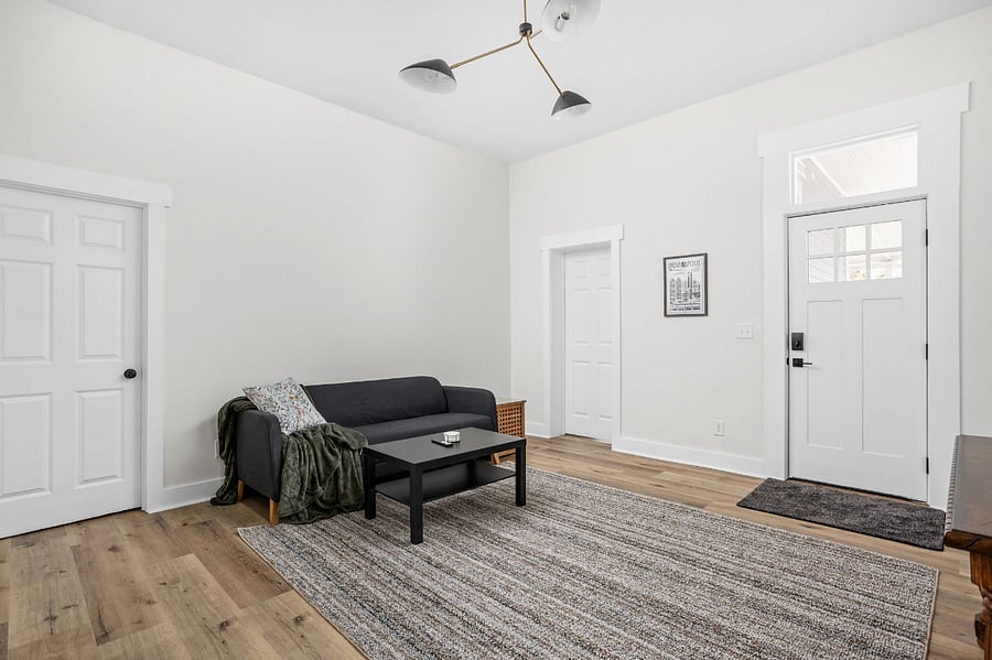 Bright and minimalist living space featuring a black sofa, modern coffee table, and neutral-toned decor with hardwood flooring.