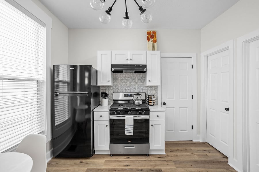 Modern kitchen with white cabinetry, a black refrigerator, and a sleek gas stove, complemented by a stylish backsplash and warm wood flooring.