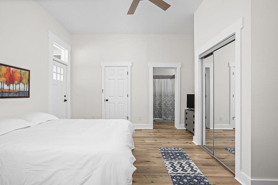 Spacious and modern bedroom with a minimalist design, featuring a large bed, mirrored closet, and en-suite bathroom access.
