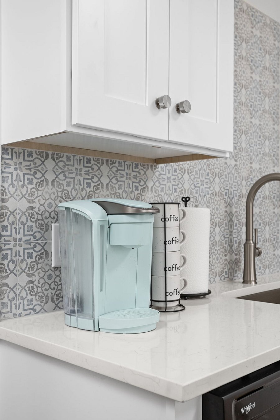 Stylish kitchen corner featuring a light blue coffee maker, patterned backsplash, and neatly organized coffee mugs.