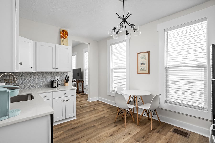 Bright and stylish kitchen with white cabinetry, a patterned backsplash, and a cozy dining nook by large windows.