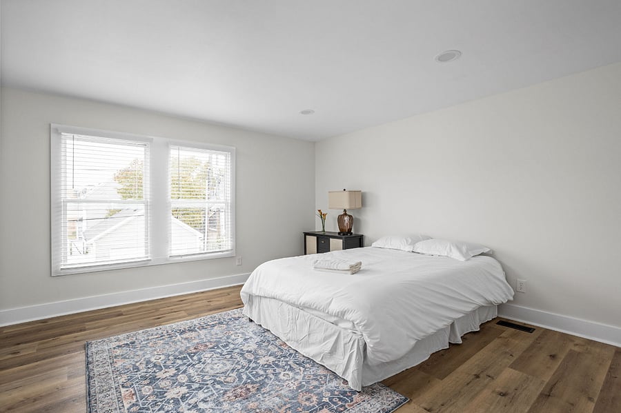 Bright and spacious bedroom featuring a cozy bed, large windows for natural light, and a stylish area rug for warmth.