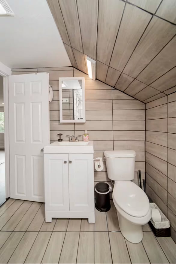 This unique bathroom is meant to be a wet room. Towel storage underneath sink, with additional room for toiletries above the sink and cabinet to the left.