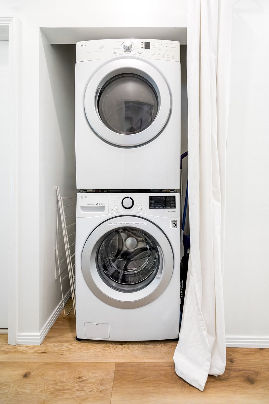 Convenient laundry nook equipped with washer/dryer, drying rack, vacuum, Swiffer, and broom.