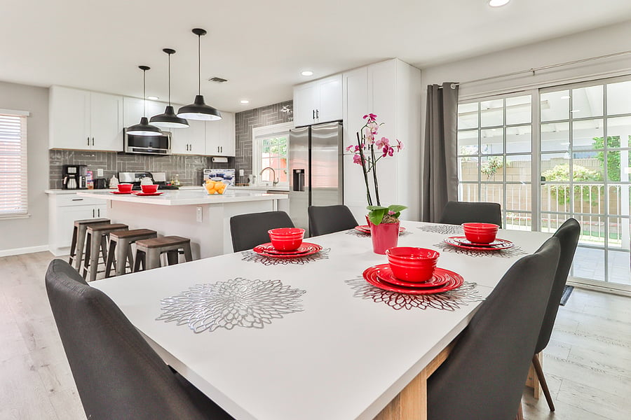 where a modern dining table with seating for six is perfectly situated between a fully equipped white kitchen with a central island and sliding glass doors that flood the space with natural light.
