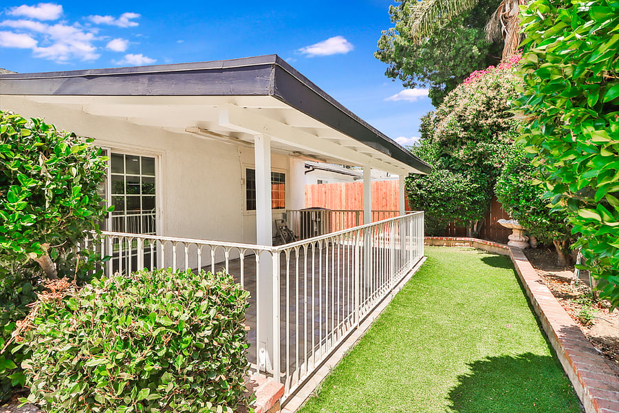 Unwind in the serene outdoor space of this featuring a covered patio with white railings, a strip of artificial grass perfect for lounging, and lush surrounding greenery for a private and relaxing atmosphere.