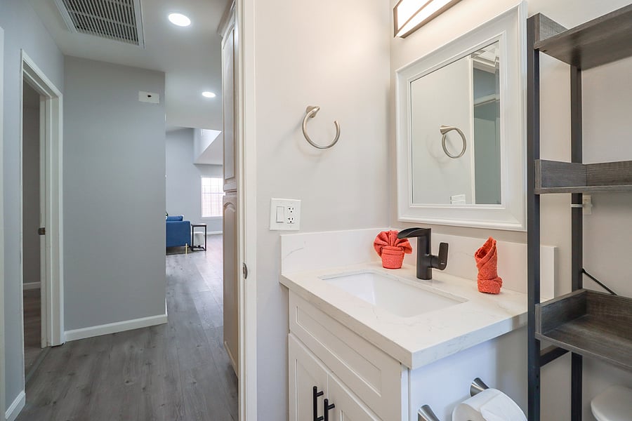 A modern and bright bathroom featuring a sleek vanity and convenient shelving awaits your use.