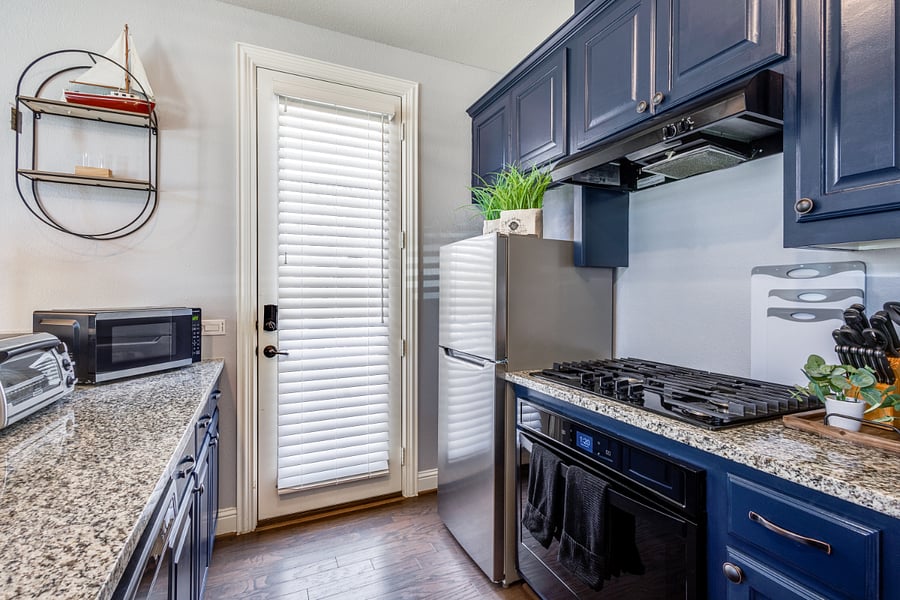 Stainless steel refrigerator with freezer, 4 burner gas stove with vent hood, single oven, and upper blue cabinets stored with dishes and glasses. Pantry stocked with ice maker, crock-pot, air fryer, along with other kitchen and cooking essentials.