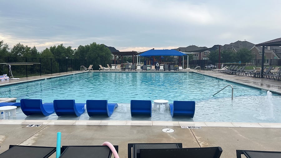 Large community outdoor swimming pool with lounge chairs, umbrellas, tables, and covered patios for shade. Guests will receive pool key card during pool season.
