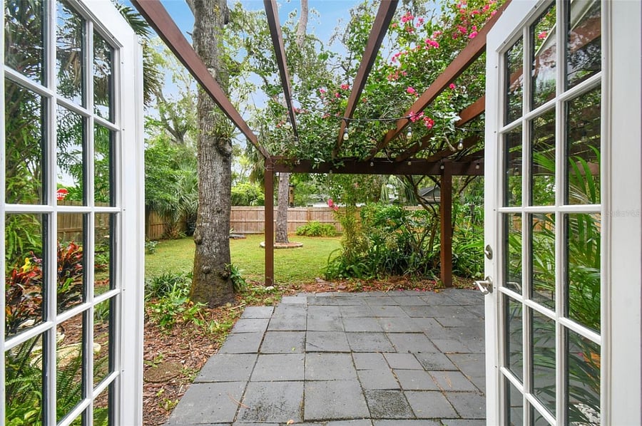 Enchanting outdoor living space accessed through French doors showcases a charming pergola-covered patio surrounded by lush landscaping.