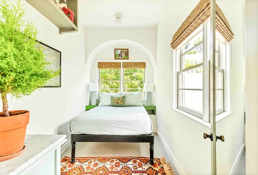 Main Bedroom with a double bed nestled in an arched alcove and organic lighting from double hung wood windows.