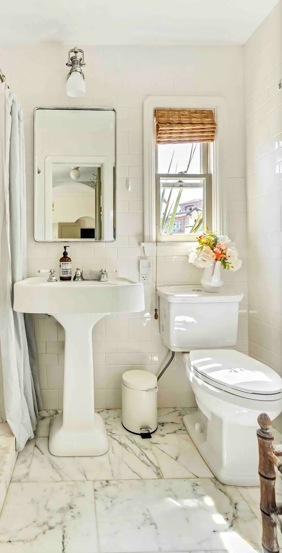 Newly renovated bathroom completely tiled from floor to ceiling showing a pedestal sink and medicine cabinet.