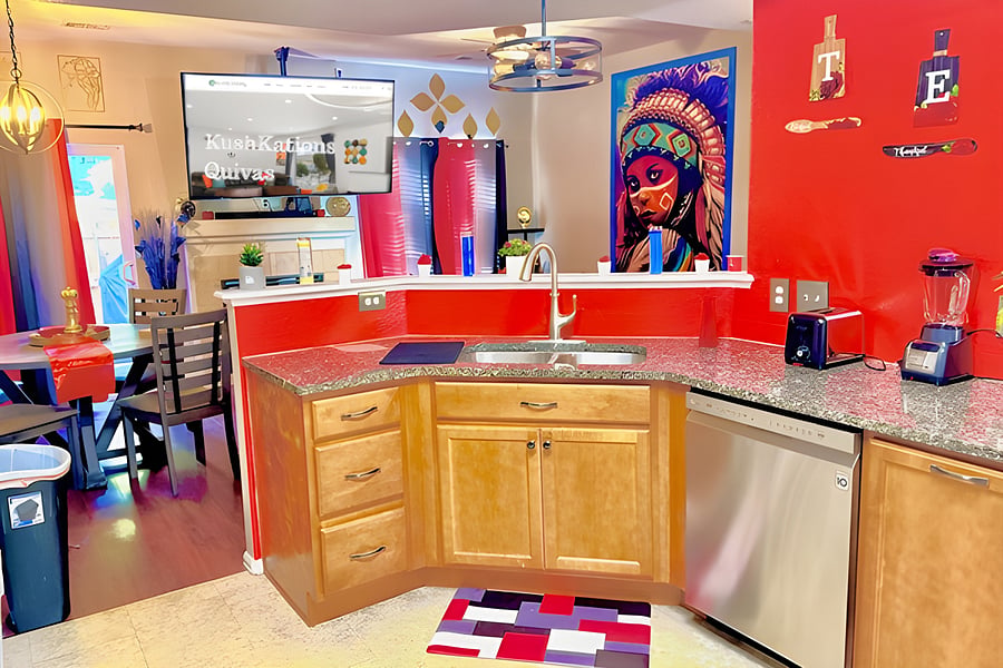 The vibrant red kitchen, with warm wood tones, offers an inviting atmosphere enhanced by a large flat-screen TV & a captivating Native American painting. 