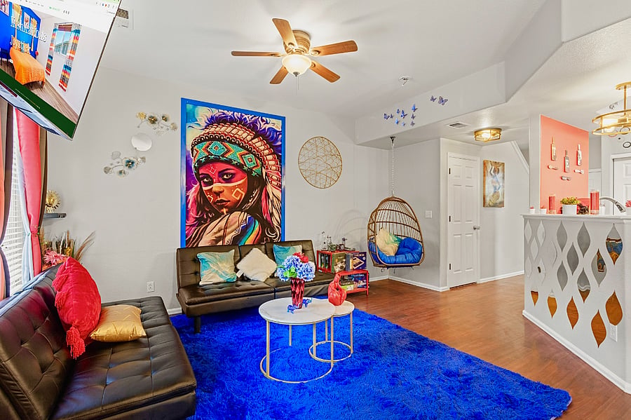 Spacious and eclectic living room with a cozy seating area, a unique hanging chair, and a vibrant Native American-inspired tapestry. Perfect for relaxing and unwinding.