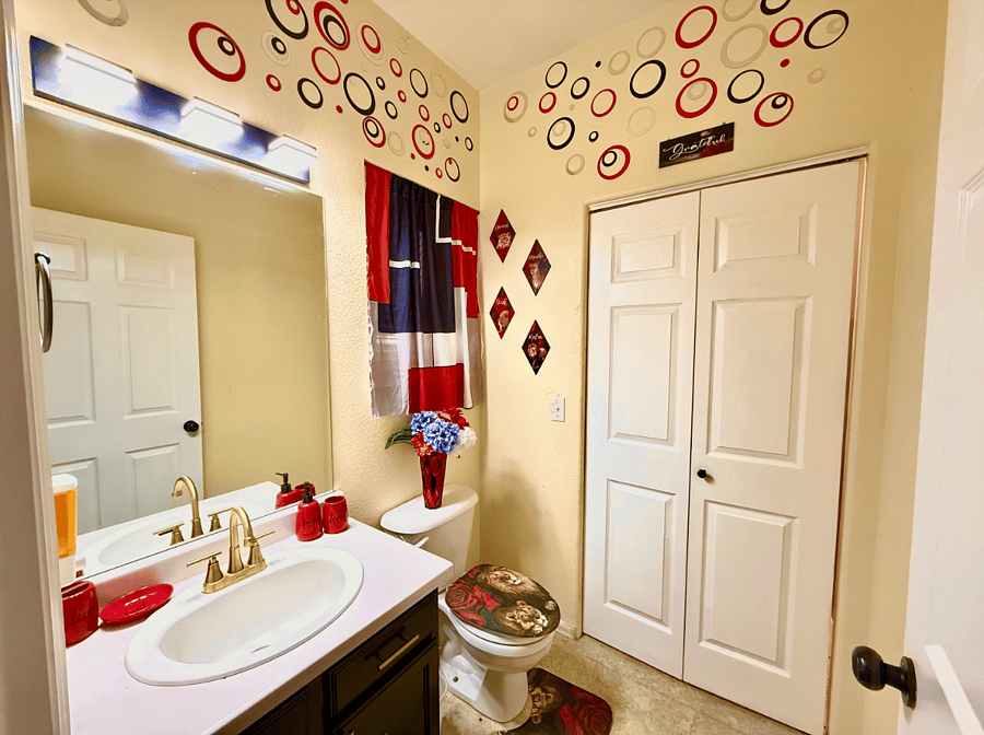 This stylish half bathroom offers a touch of luxury in a compact space. Adorned with red unique accent pieces, its the perfect spot for a quick freshen-up. Plus, with convenient access to the laundry room, you can easily keep your clothes fresh and tidy.