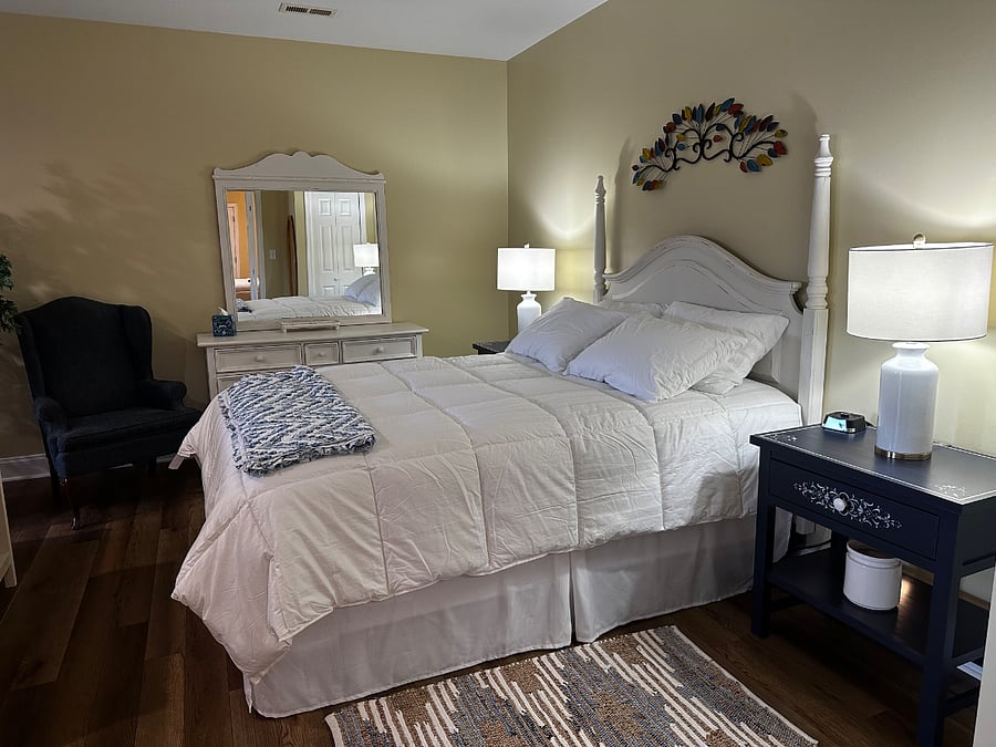 Master bedroom with queen bed, side tables and lamps, dresser, clothes closet, and wingback chair. Open to the master living room with fireplace.