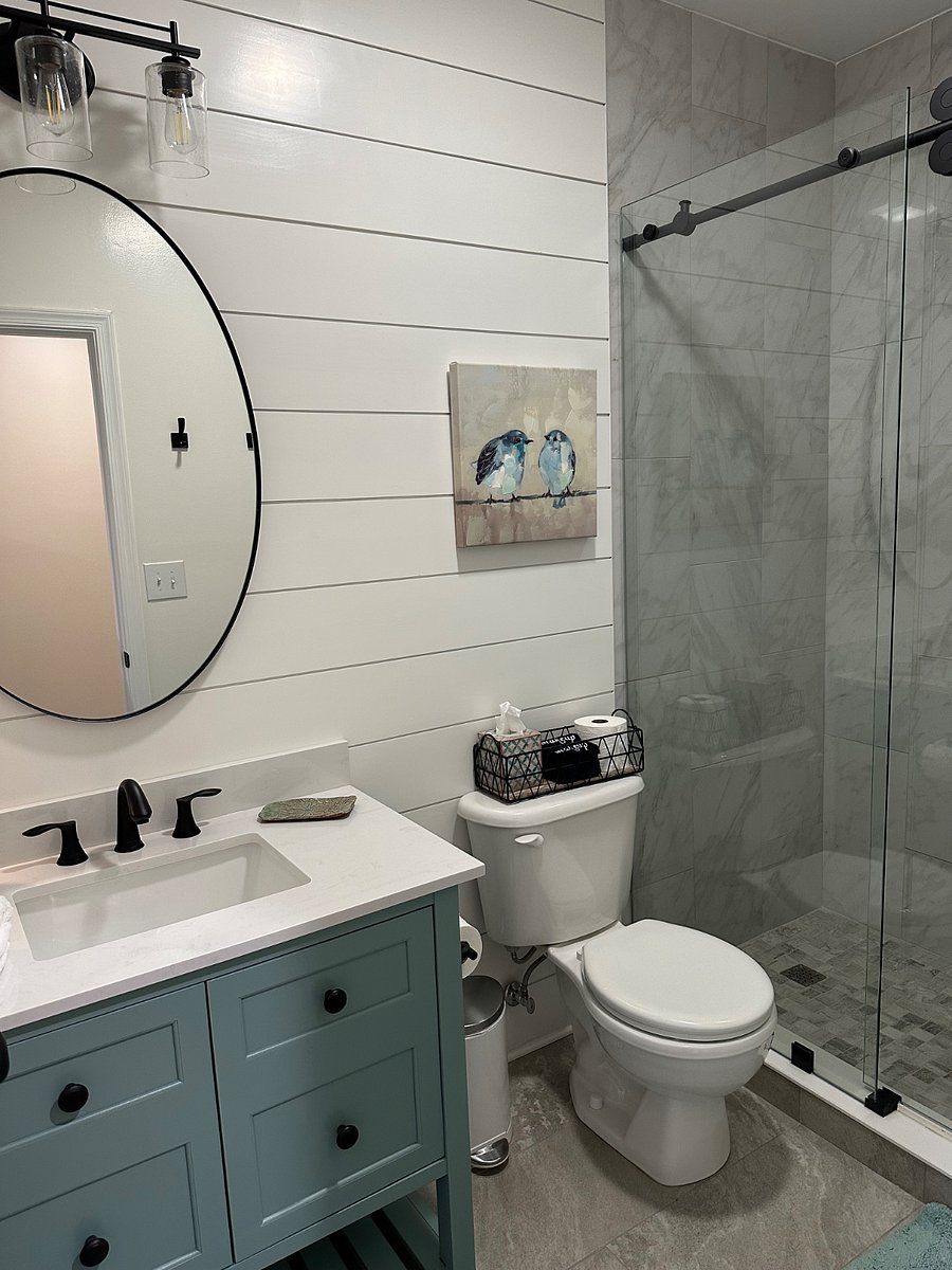 Bathroom shiplap wall, ceramic tiled floor, and tiled shower with rain shower head.