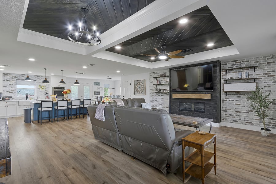 The living room offers a large genuine leather sofa and loveseat, 70" Smart TV, and an electric fireplace with an open floor plan to the island and kitchen seating
